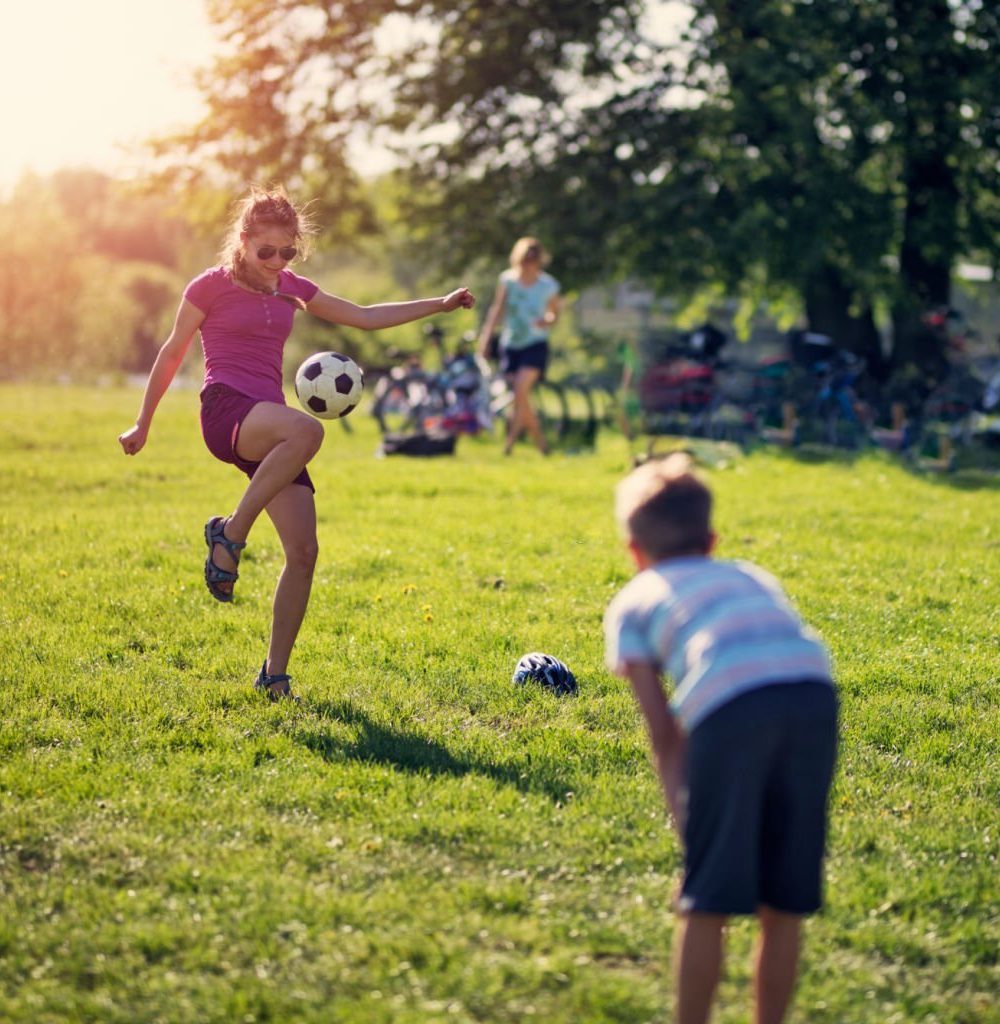Teenage girl playing soccer with her brother. Mother visible in the background.
Nikon D850