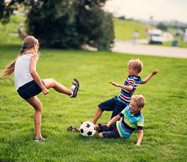 Three kids playing football on grass. Summer day. Sister and two brothers are running aggressively for the ball.
Nikon D810